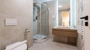 A modern bathroom with a glass-enclosed shower, a toilet, and a vanity with a mirror. - LimeTree Residence by BQA (Budapest)