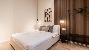 A modern bedroom with a bed, bedside tables, a wall-mounted light fixture, and a wooden panel wall.