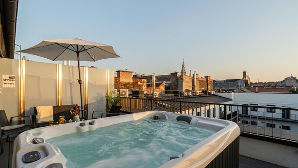 A hot tub with a city view, a table with chairs, and an umbrella. - LimeTree Residence by BQA (Budapest)