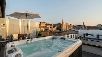 A hot tub with a city view, a table with chairs, and an umbrella.