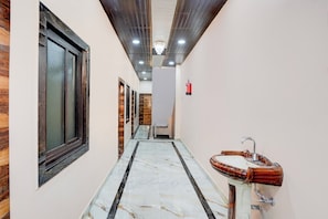 A hallway with a marble floor, a wooden door, and a sink with a wooden basin. - Super OYO Hotel O Tedhi Bazaar (Ayodhya)