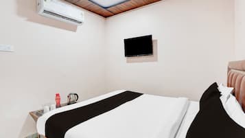 Habitación de hotel con cama, televisor montado en la pared, aire acondicionado y una pequeña mesa con tetera y tazas.