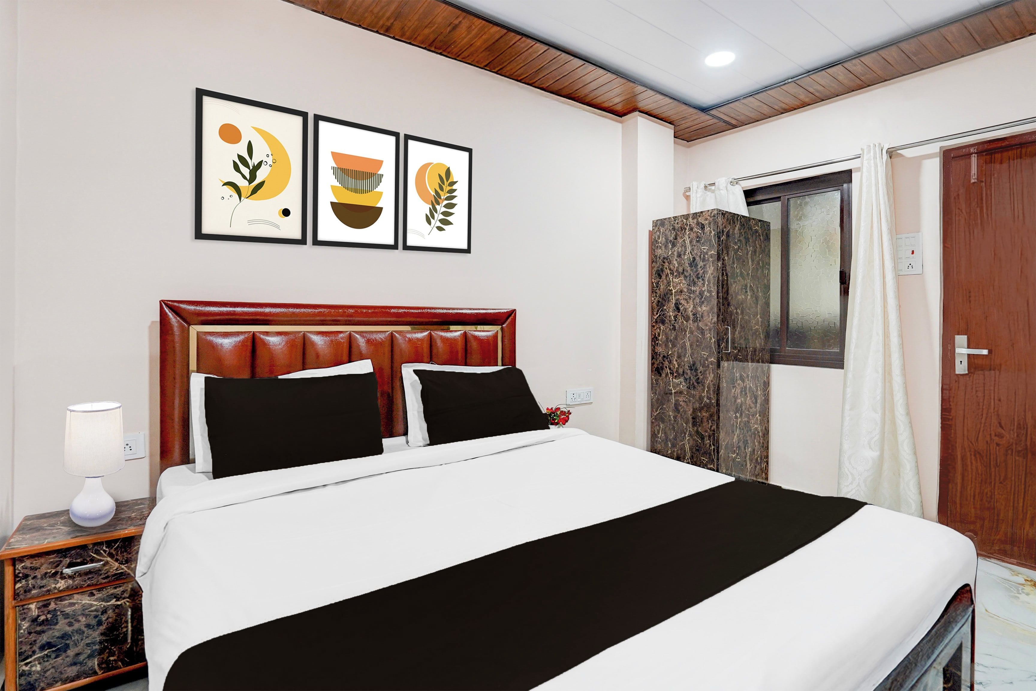 Habitación de hotel con cama, mesita de noche, lámpara y tres cuadros en la pared.