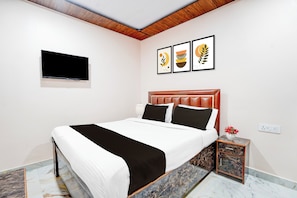 Un dormitorio moderno con una cama, un televisor montado en la pared y una mesita de noche con un jarrón de flores.