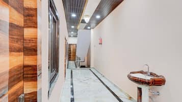 Un pasillo con suelo de mármol, una pared de madera a la izquierda y un baño con lavabo y espejo a la derecha.