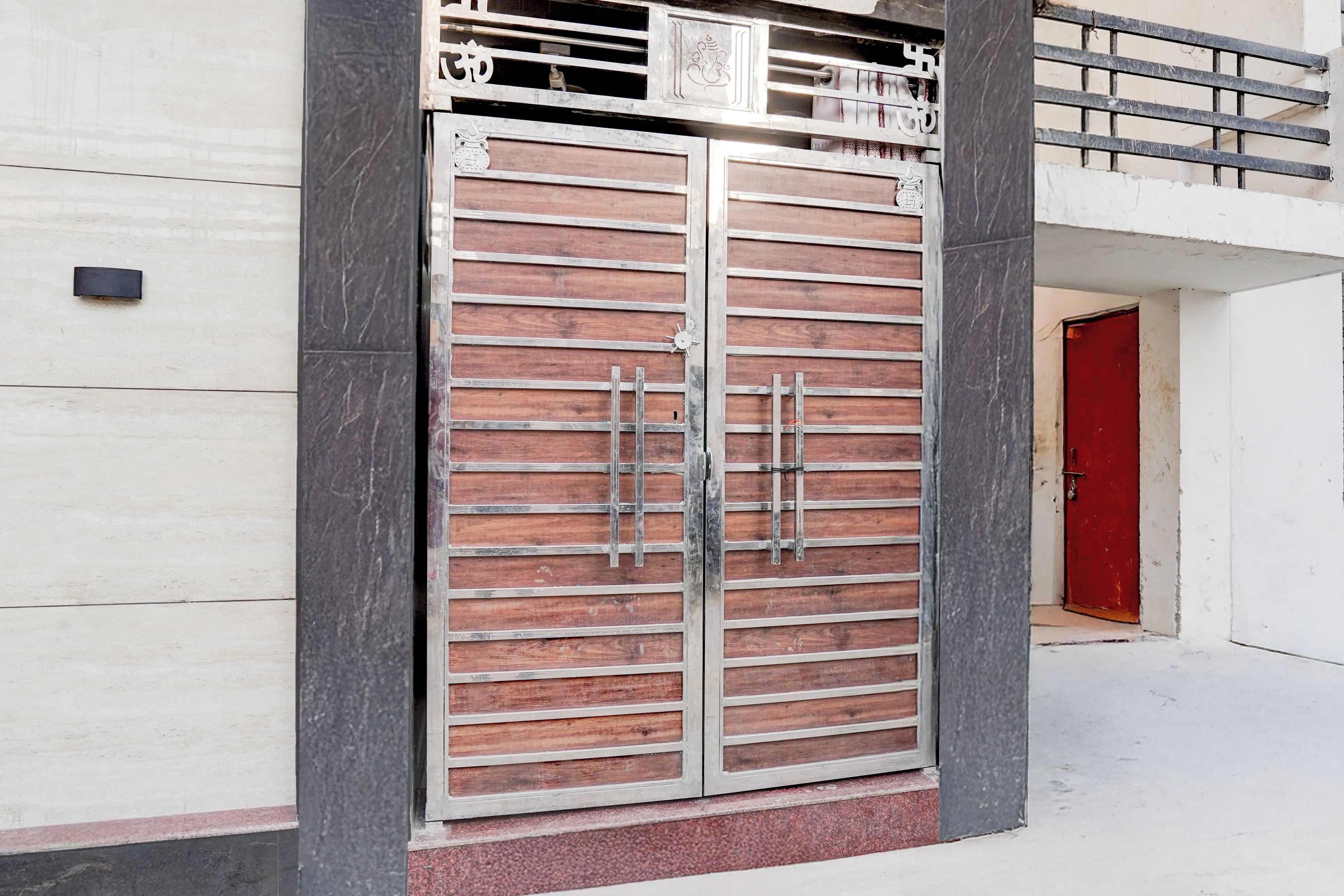 Una entrada amplia con puertas dobles, un marco metálico y paneles de madera, integrada en un edificio moderno de fachada blanca y una puerta roja al fondo.