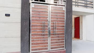 Una entrada amplia con puertas dobles, un marco metálico y paneles de madera, integrada en un edificio moderno de fachada blanca y una puerta roja al fondo.