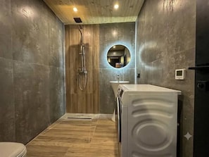 A modern bathroom with a wooden shower enclosure, a built-in washing machine, and a round mirror.