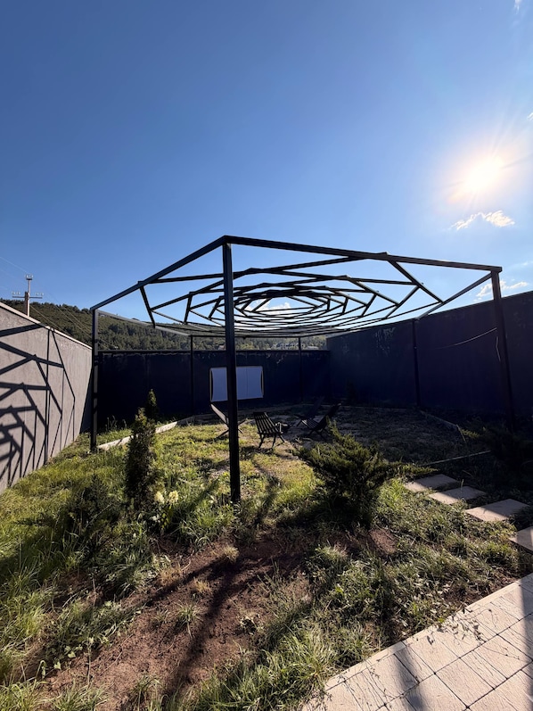 A geometric metal structure in an outdoor setting with grass and a clear sky.