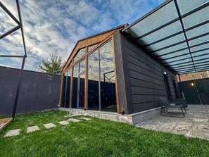 Ein modernes Haus mit einem großen Glasfenster, einem Holzdach und einer gepflasterten Terrasse.