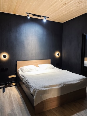 A modern bedroom with a wooden headboard, a bed with white bedding, and two wall-mounted lights.