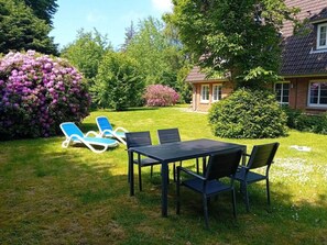 A garden with a table and chairs, a lawn, and a house in the background. - Holiday Apartment in Nebel With Swimming Pool (Nebel)