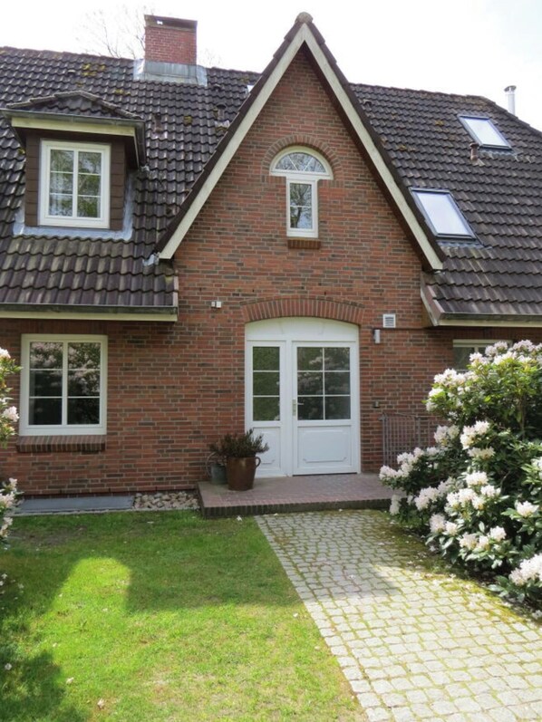 A two-story brick house with a central entrance, two windows on the ground floor, and a small garden area with a paved walkway. - Holiday Apartment in Nebel With Swimming Pool (Nebel)