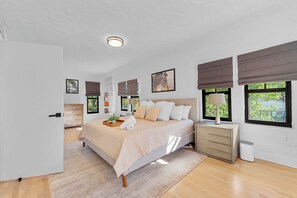 Ein Schlafzimmer mit Bett, Nachttischen, einer Lampe und einem Fenster mit Blick auf Grünflächen.