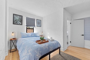 A bedroom with a large bed, a wooden bench, two bedside tables, and a door leading to another room. - 4BR Pool Home w/ Private Guest Suite – West Palm Beach (West Palm Beach)