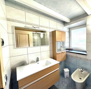 Un baño con tocador de madera, un lavamanos, un espejo, cabina de ducha y un bidé.