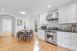 A modern kitchen with white cabinets, a stainless steel stove, and a dining area with wooden chairs and a table. - Tropical 3BR Oasis w/ Pool (West Palm Beach)
