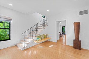 En modern inredning med en trätrappa, vita väggar och ett stort fönster med utsikt över grönområden.