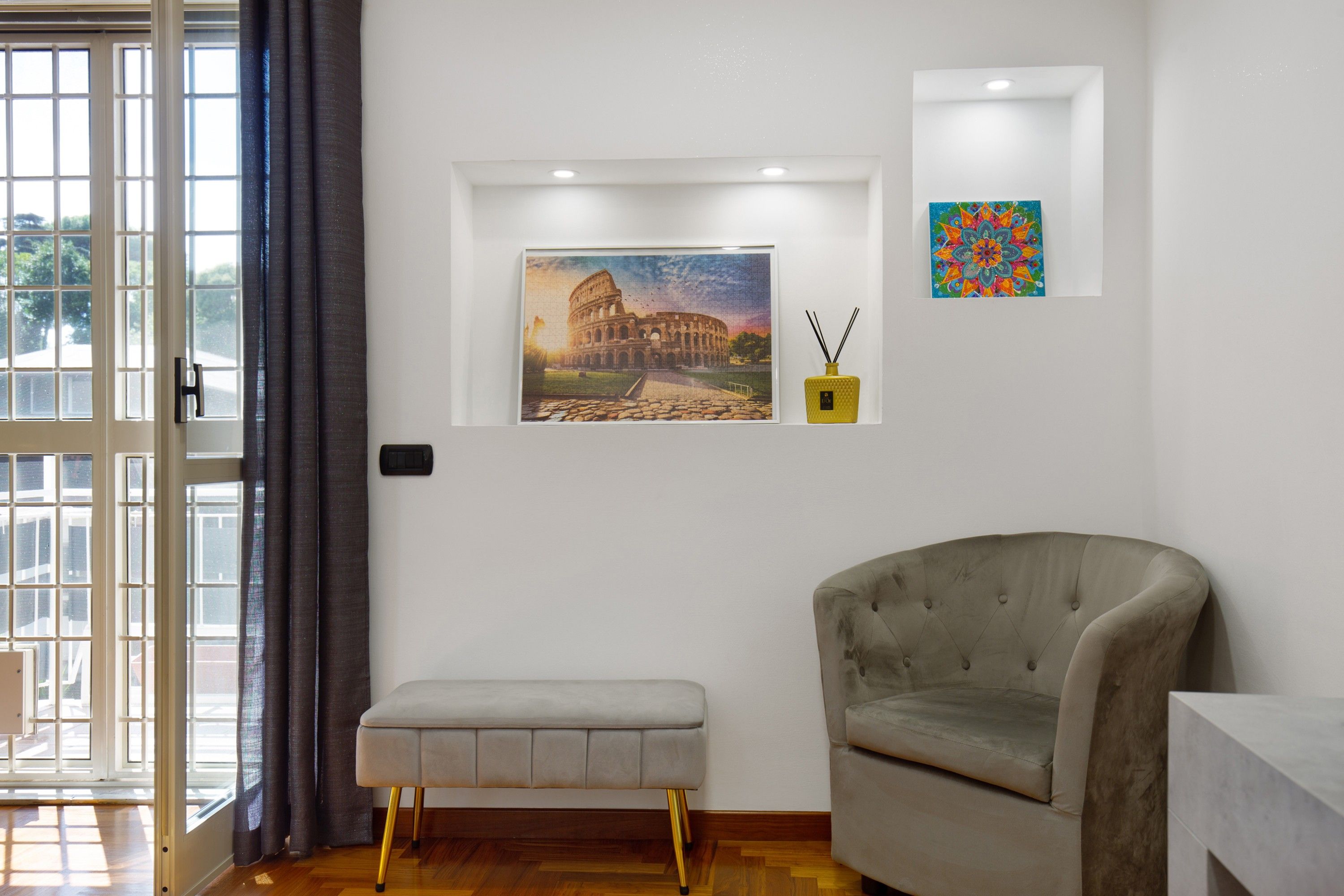 A room with a bench, a chair, a picture of the Colosseum, and a decorative item on the wall.