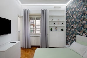 A bedroom with a bed, a TV, a wardrobe, a radiator, and a window with curtains. - Alice’s House Apartment with Balcony, Wi-Fi, and Air Conditioning (Roma)