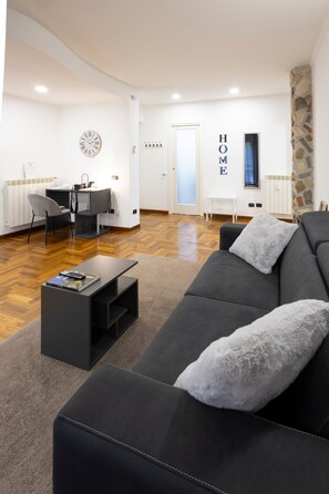 A modern living room with a black sofa, a coffee table, and a dining area with a chair and table. - Alice’s House Apartment with Balcony, Wi-Fi, and Air Conditioning (Roma)