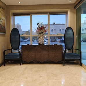 A reception area with a bench, a vase with flowers, and a view of the street through large windows. - Manazilna Serviced Apartments (Riyadh)