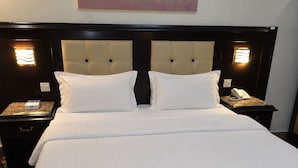 A hotel room with a large bed, two bedside tables, a wall-mounted telephone, and a painting above the bed. - Manazilna Serviced Apartments (Riyadh)