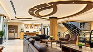A modern lobby with a reception desk, leather seating, a staircase, and a marble floor. - Manazilna Serviced Apartments (Riyadh)