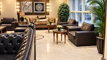 A modern living room with a sectional sofa, armchairs, and a coffee table. There are decorative wall art pieces and a large potted plant.