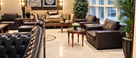 A modern living room with a sectional sofa, armchairs, and a coffee table. There are decorative wall art pieces and a large potted plant.