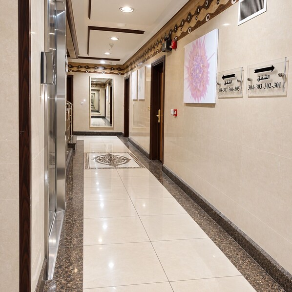 A hotel corridor with a marble floor, directional signs, and a large floral artwork on the wall. - Manazilna Serviced Apartments (Riyadh)