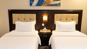 A hotel room with two beds, a nightstand with a lamp, and a patterned carpet. - Manazilna Serviced Apartments (Riyadh)