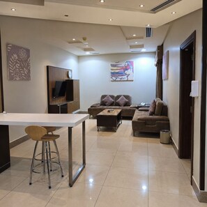 A modern living room with a sofa, a coffee table, and a TV. - Manazilna Serviced Apartments (Riyadh)