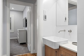 A modern bathroom with a white sink, wooden cabinet, and a mirror.