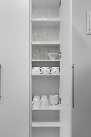 Un interior blanc amb un moble que conté vidrieria, plats i tasses.