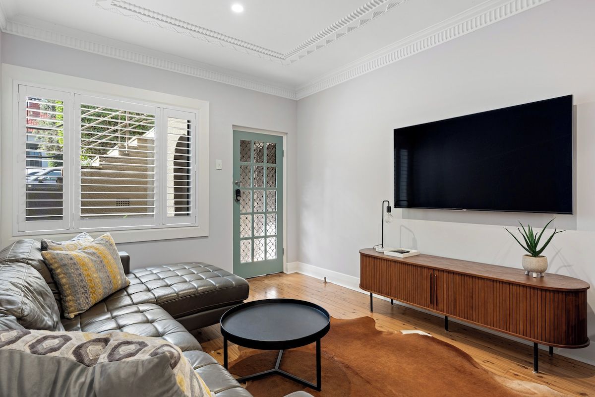 A modern living room with a leather sofa, a round coffee table, a wooden console table, and a large flat-screen TV mounted on the wall.