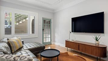 A modern living room with a leather sofa, a round coffee table, a wooden console table, and a large flat-screen TV mounted on the wall.