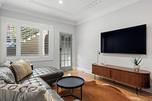 A modern living room with a leather sofa, a round coffee table, a wooden console table, and a large flat-screen TV mounted on the wall.