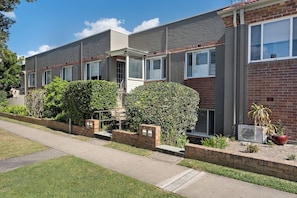 A row of townhouses with a paved driveway, brick walls, and a small garden area with plants.