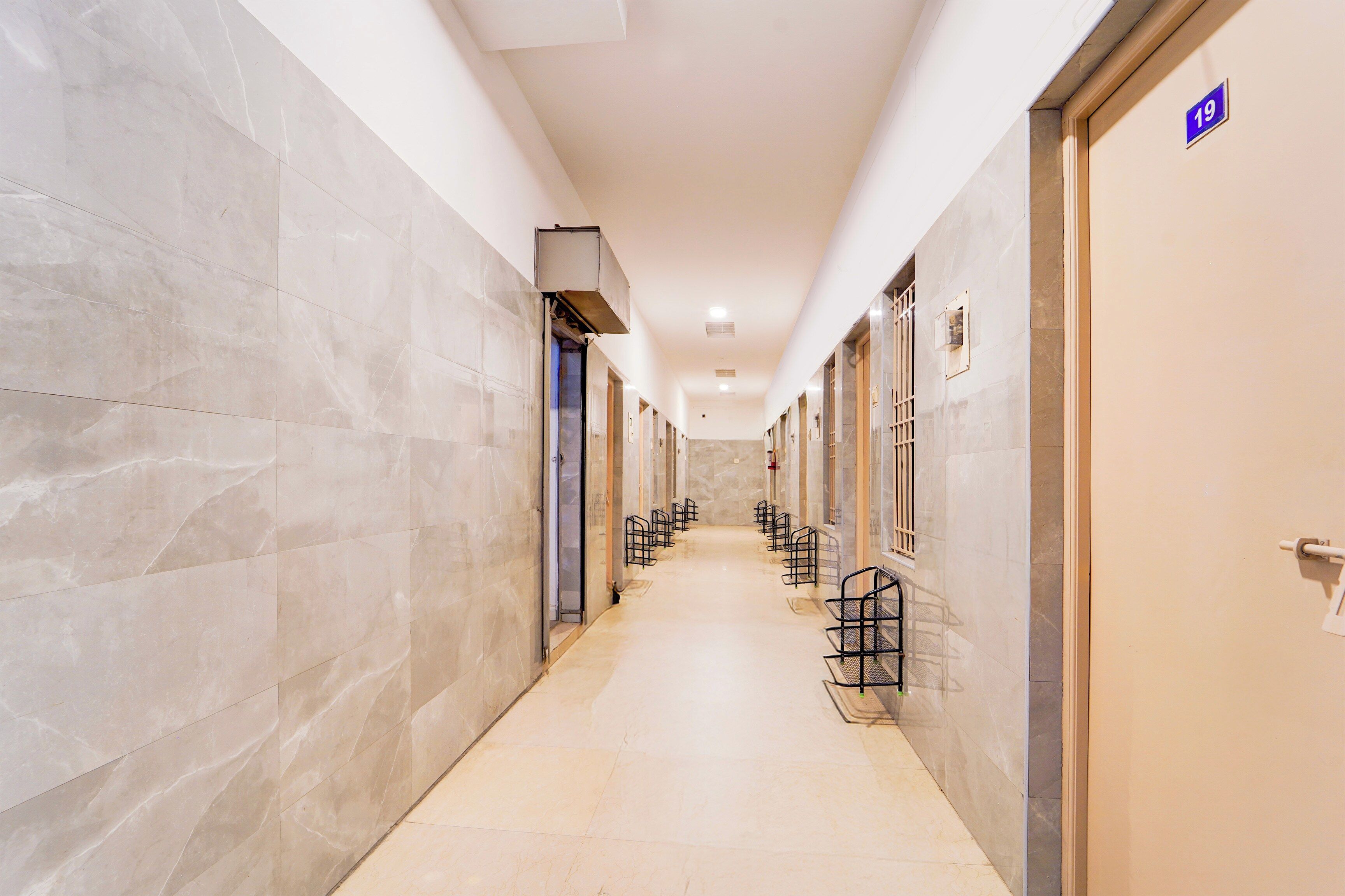 Un pasillo de hotel con paredes de mármol, suelo de baldosas y puertas con números de habitación.