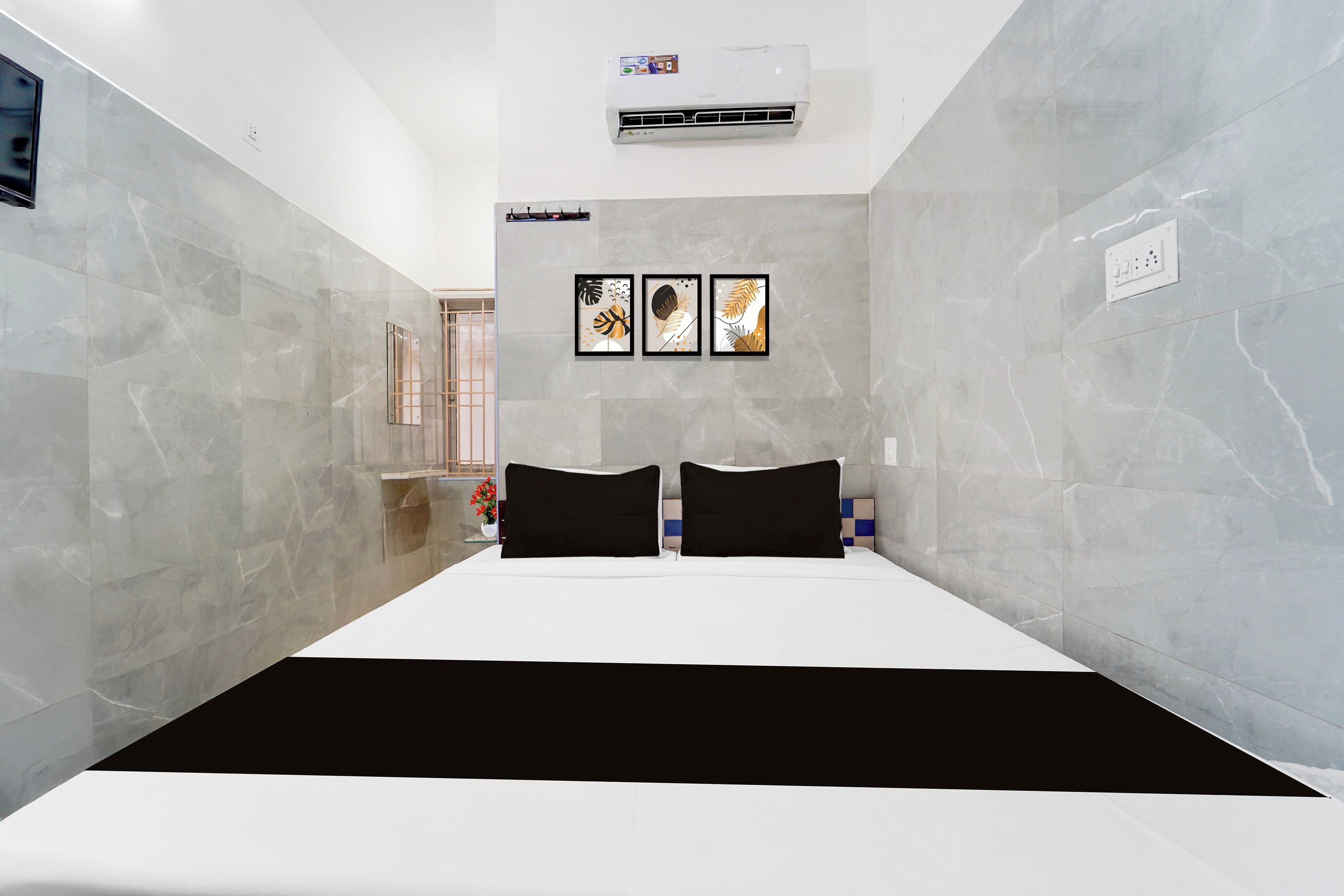 Une chambre d’hôtel avec un lit, un climatiseur fixé au mur et trois œuvres d’art encadrées au-dessus du lit.