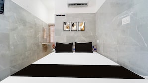 Quarto de hotel com uma cama, ar condicionado fixado na parede e três obras de arte emolduradas acima da cama.