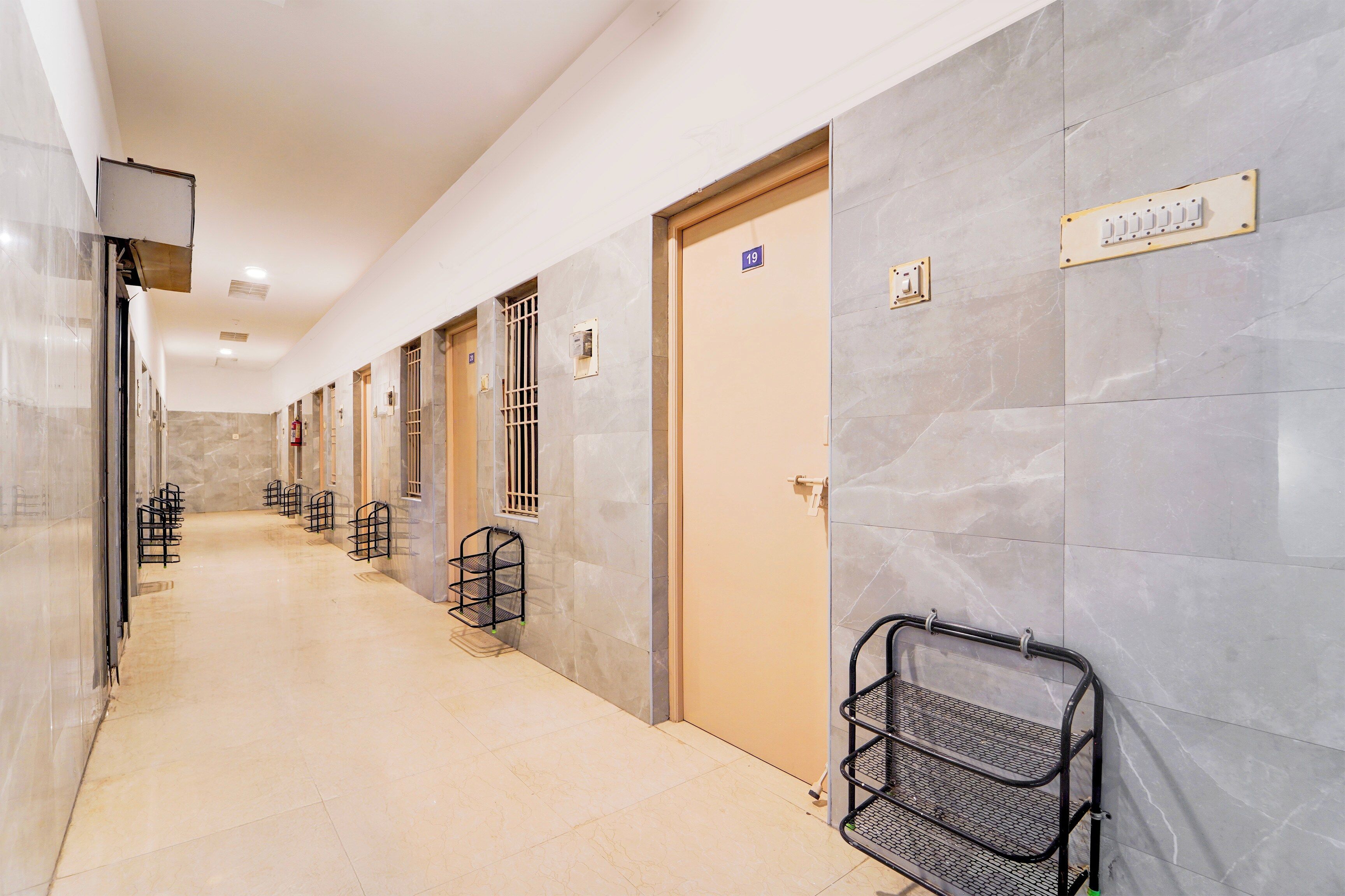 Un pasillo de hotel con paredes de mármol, puertas numeradas y estanterías metálicas.