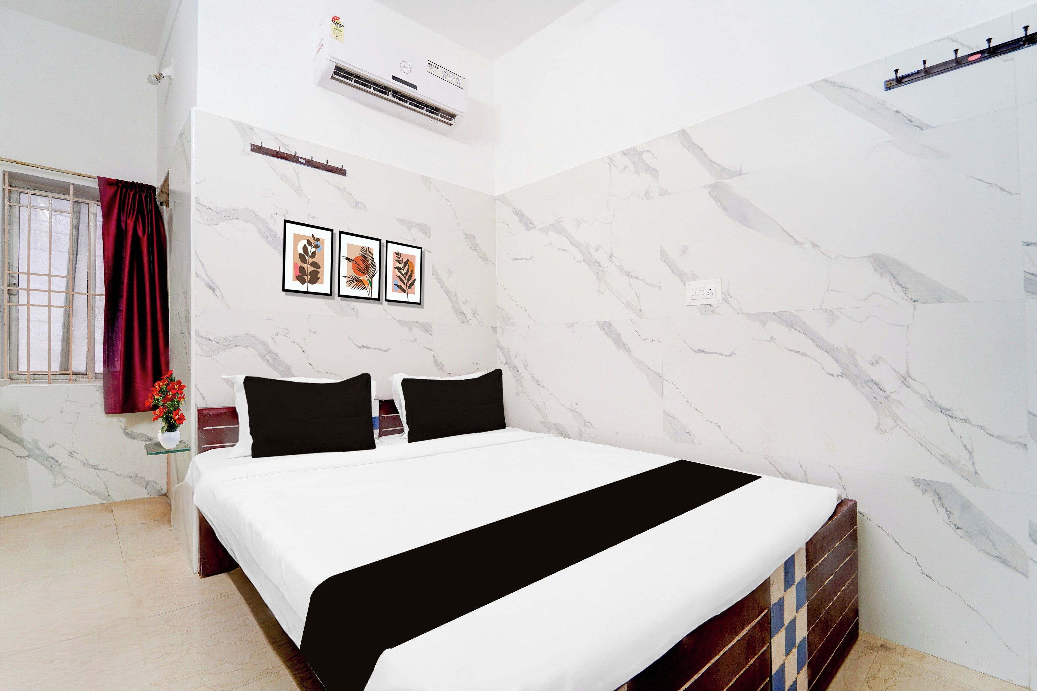 Habitación de hotel con cama, ventana con cortinas, equipo de aire acondicionado y tres cuadros en la pared.
