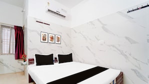 Quarto de hotel com cama, janela com cortinas, ar condicionado e três quadros na parede.