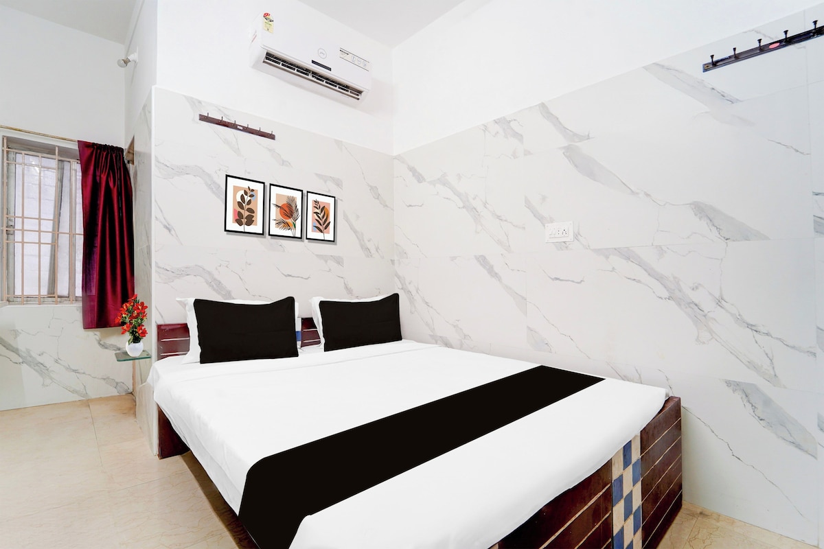 Quarto de hotel com cama, janela com cortinas, ar condicionado e três quadros na parede.