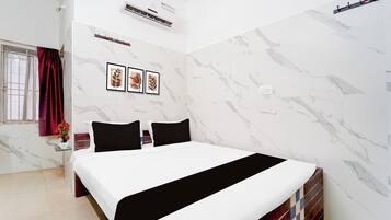 Habitación de hotel con cama, ventana con cortinas, equipo de aire acondicionado y tres cuadros en la pared.