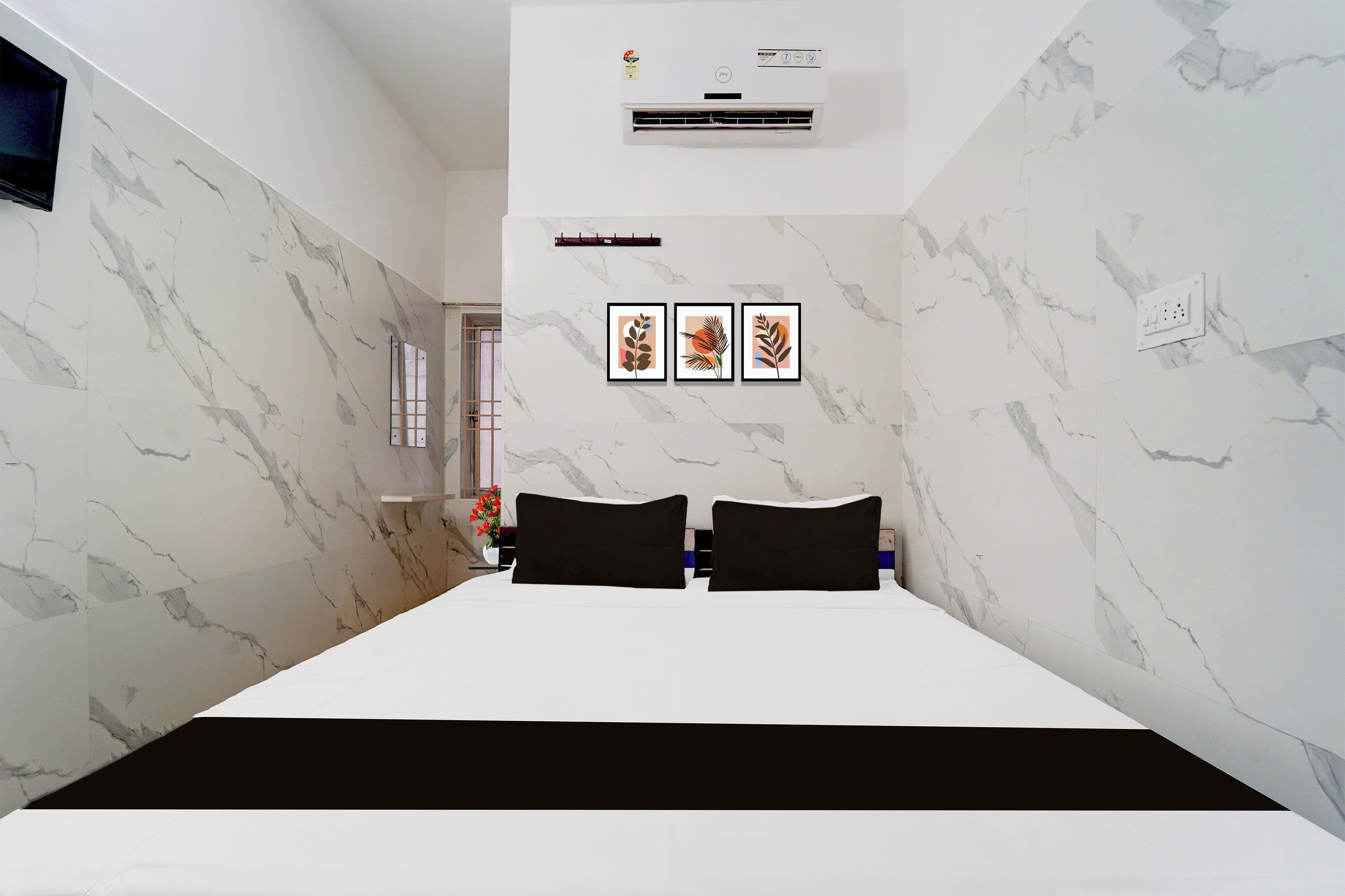 A hotel room with a bed, a wall-mounted air conditioner, and three framed pictures.