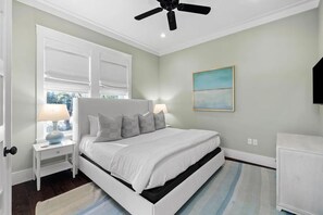 A bedroom with a bed, nightstands, a ceiling fan, a window with blinds, a painting, and a cabinet.