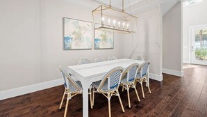 Un comedor con una mesa blanca y sillas de mimbre, una araña y arte abstracto en la pared.